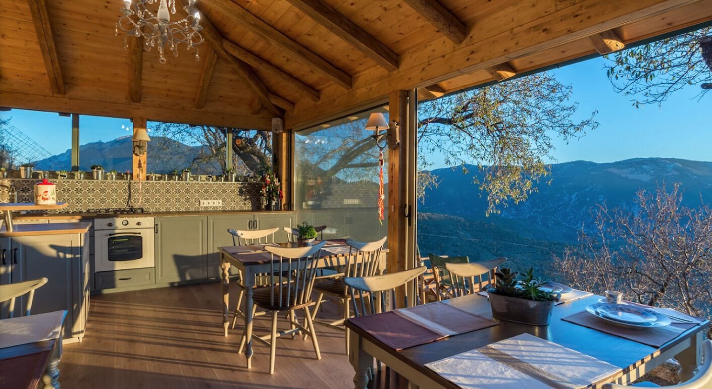 Un interior de madera con cocina y comedor, amplias ventanas con vistas a la montaña.