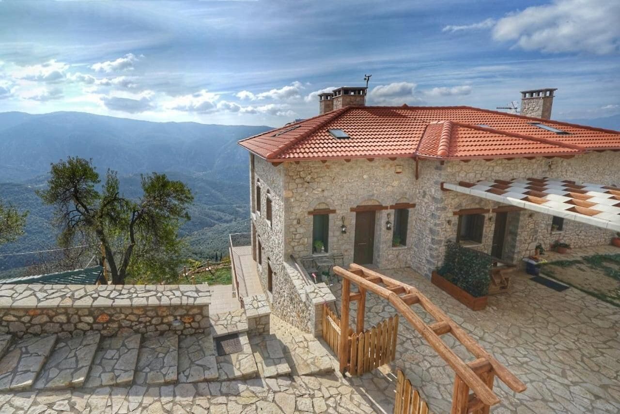A stone building with a red-tiled roof, a stone staircase, and a wooden railing.