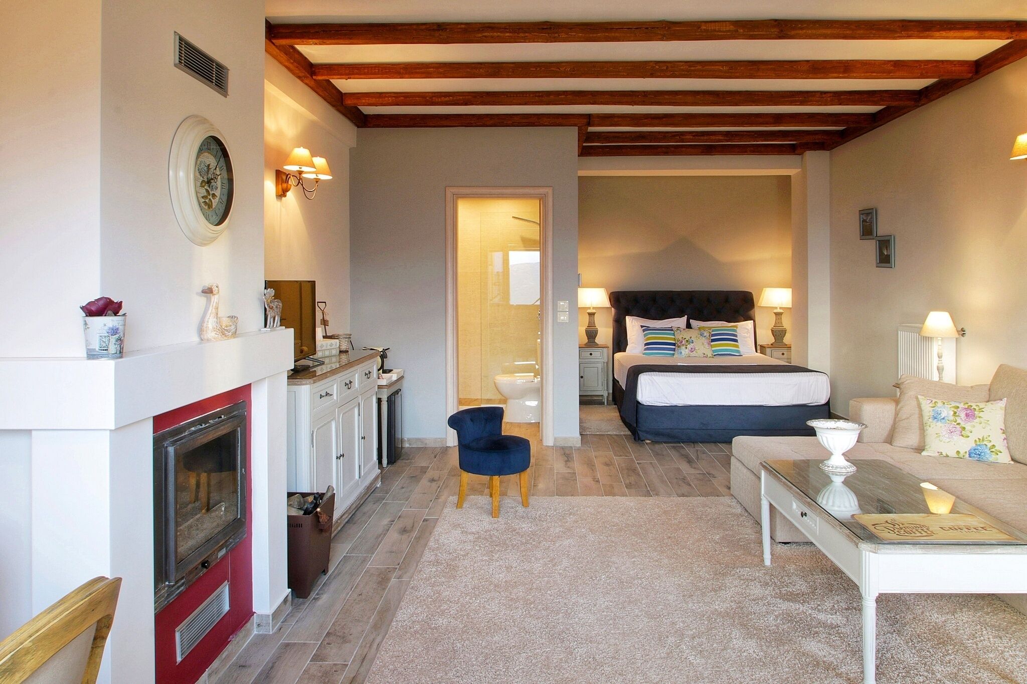 Una habitación de hotel acogedora con chimenea, una cama con almohadas, una mesita de noche y una pequeña mesa con una vela.