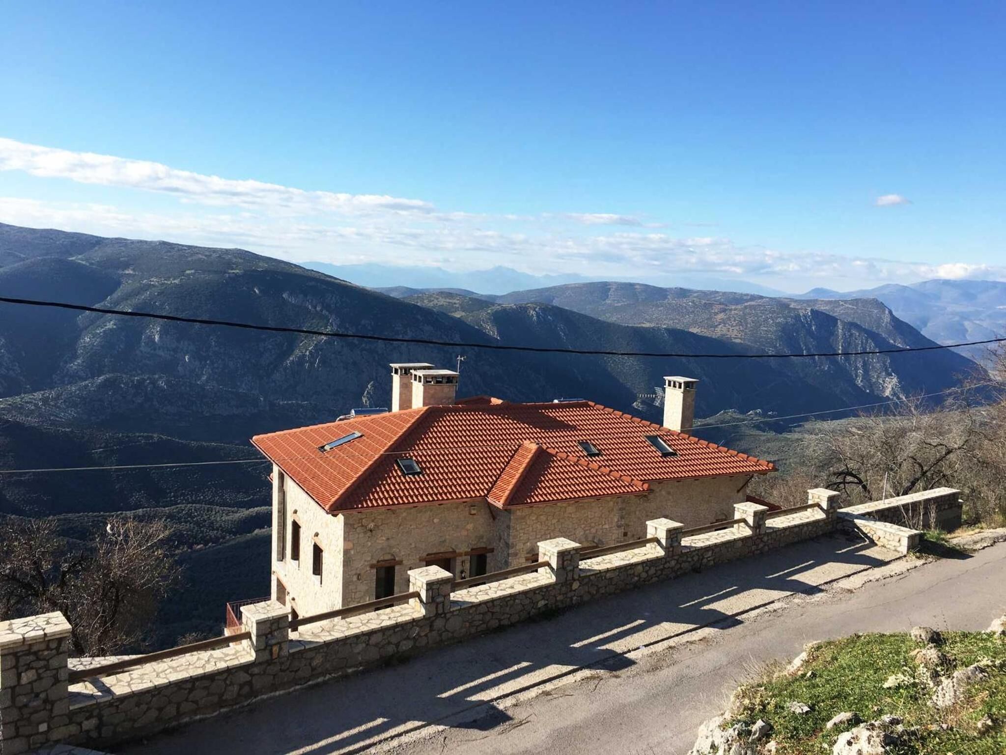 Ein Steinhaus mit rotem Ziegeldach, gelegen an einem Hang mit Blick auf Berge im Hintergrund.