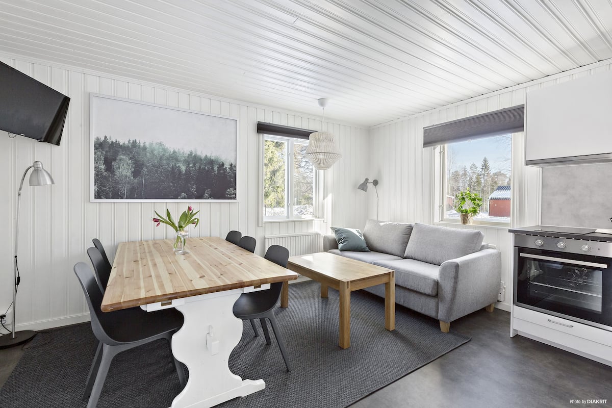 A modern kitchen with white cabinetry, a wooden dining table, and a gray sofa.