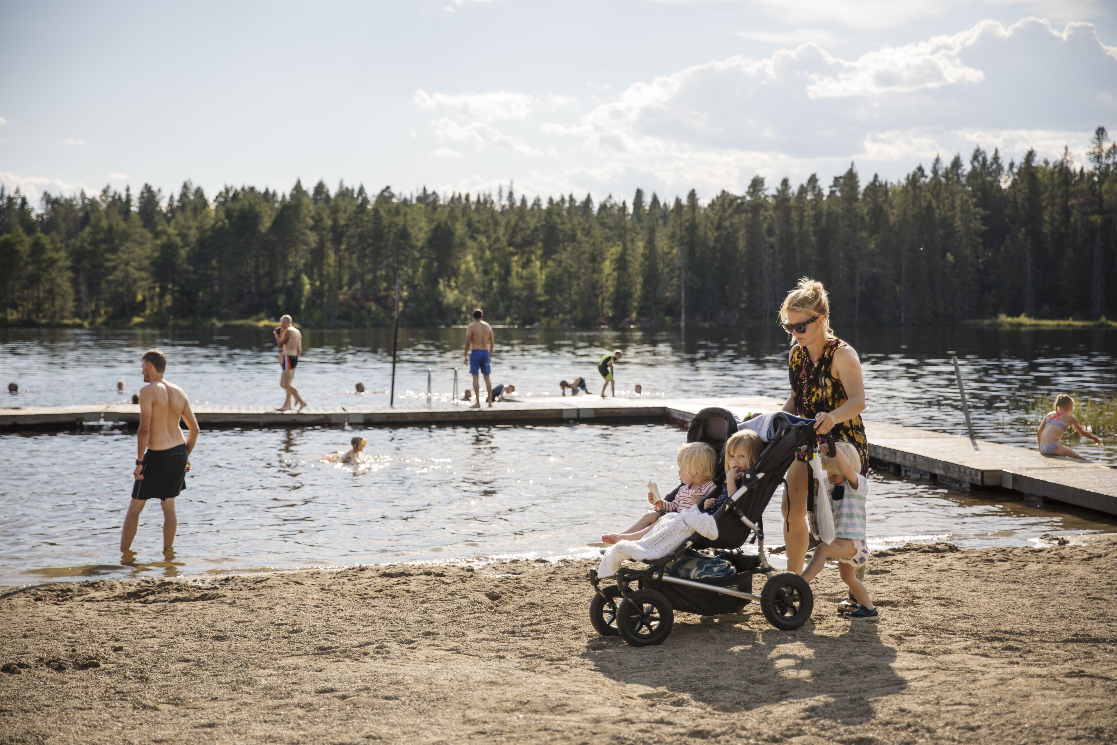 A lakeside scene with people swimming and walking along the shore.