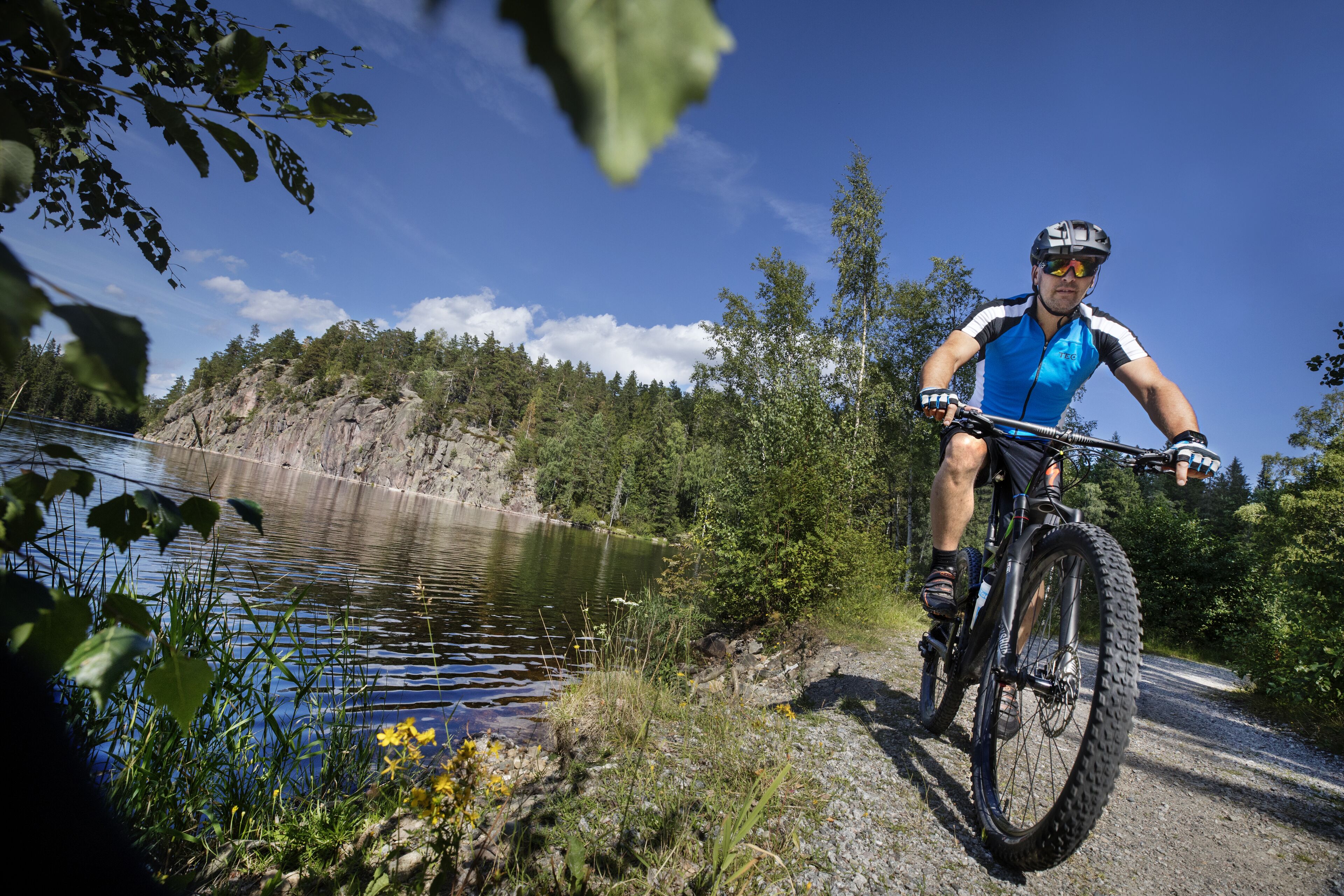 A mountain biker on a trail with a lake and forest in the background.