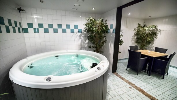 A bathroom with a hot tub, tiled walls, a wooden table with chairs, and potted plants. - First Camp Ånnaboda-Örebro (Garphyttan)