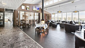A spacious restaurant with a high ceiling, wooden paneling, and large windows offering a view of the outdoors. - First Camp Ånnaboda-Örebro (Garphyttan)