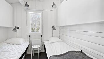 A small, white, single-room hotel room with two beds, a small table, and two bedside lamps.