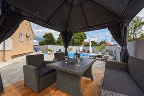 Una terrazza esterna con mobili in rattan, una piscina e un'area coperta.