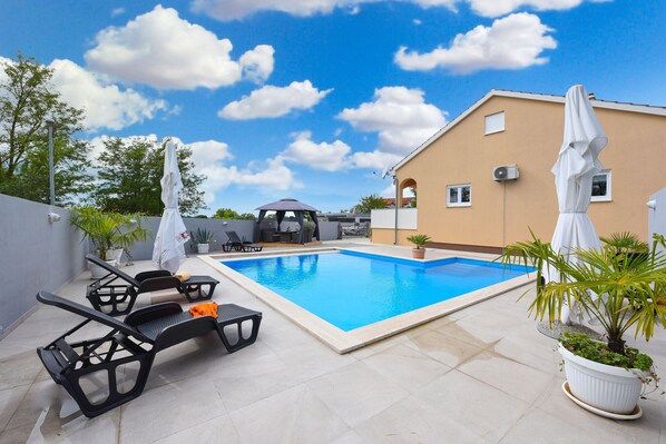 Una piscina con lettini, ombrelloni e piante in vaso.