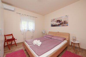 Una camera da letto con un letto, una sedia, un comodino, una ventola e un quadro appeso al muro.