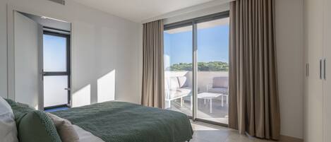 Un dormitorio moderno con una cama grande, un ventanal corredero a un balcón y vistas al exterior.