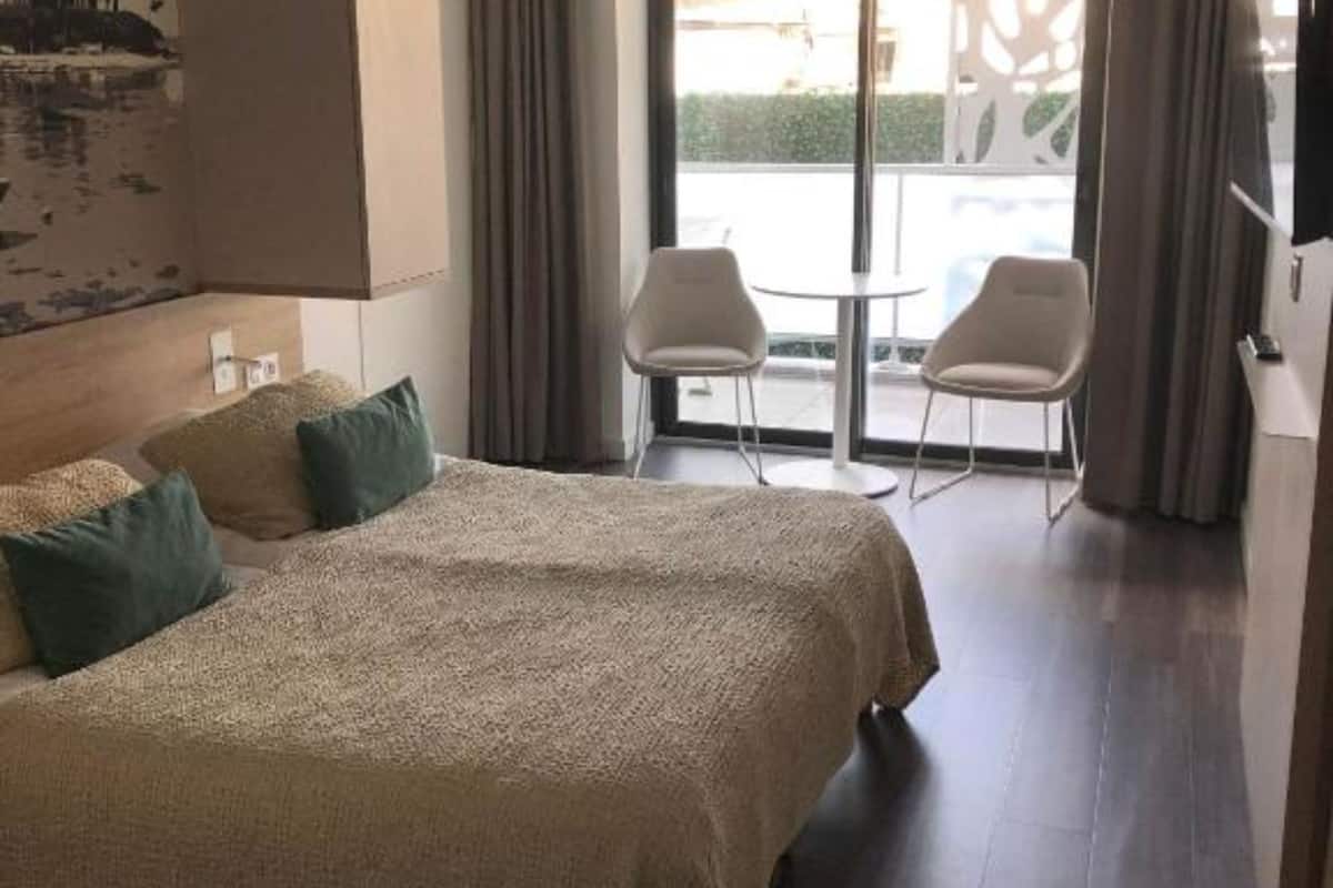 Ein Hotelzimmer mit einem großen Bett, zwei Sesseln, einem Balkon mit Aussicht und einem Bild an der Wand.