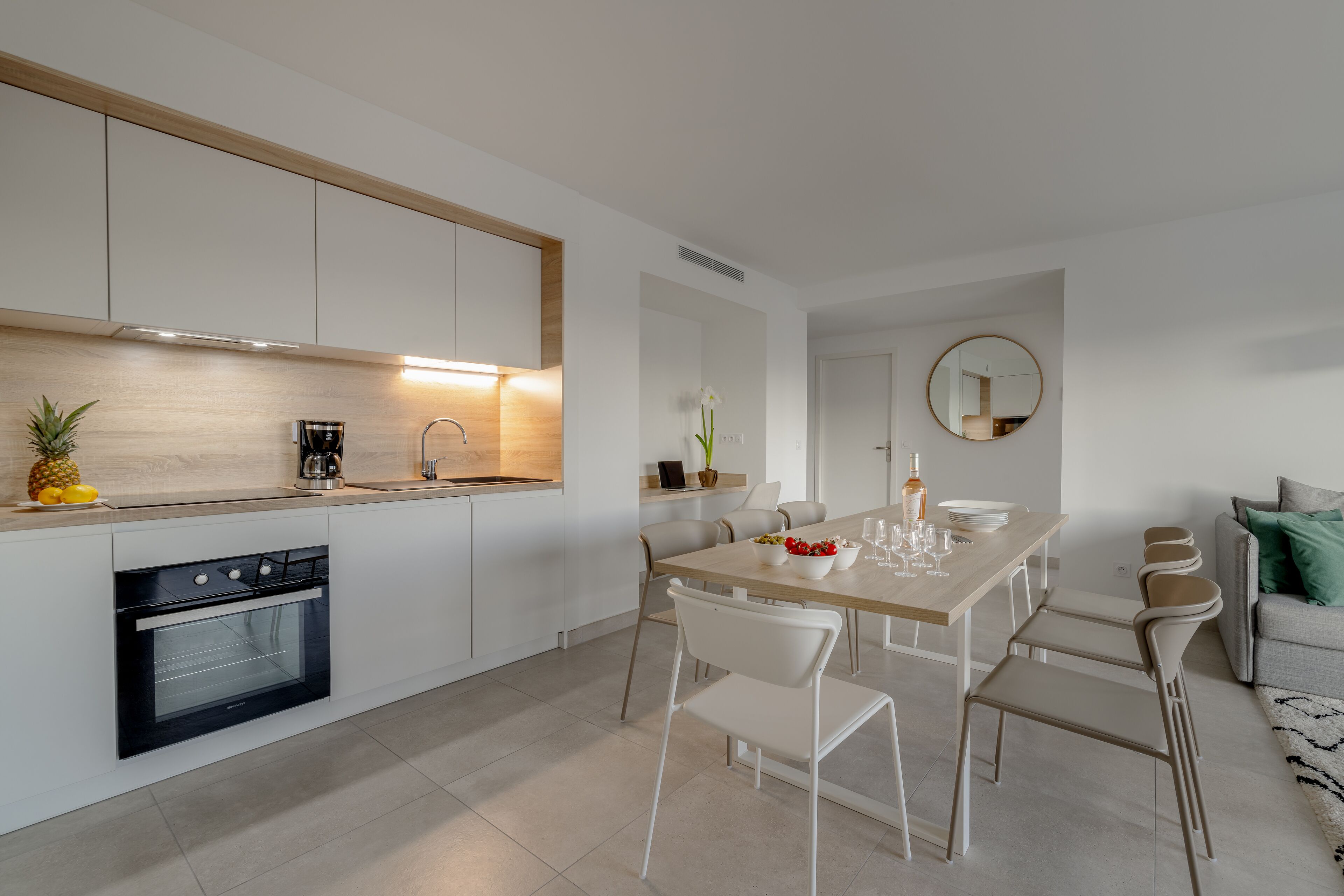 Een moderne keuken met witte kasten, een inbouwoven en een eethoek met een houten tafel en witte stoelen.
