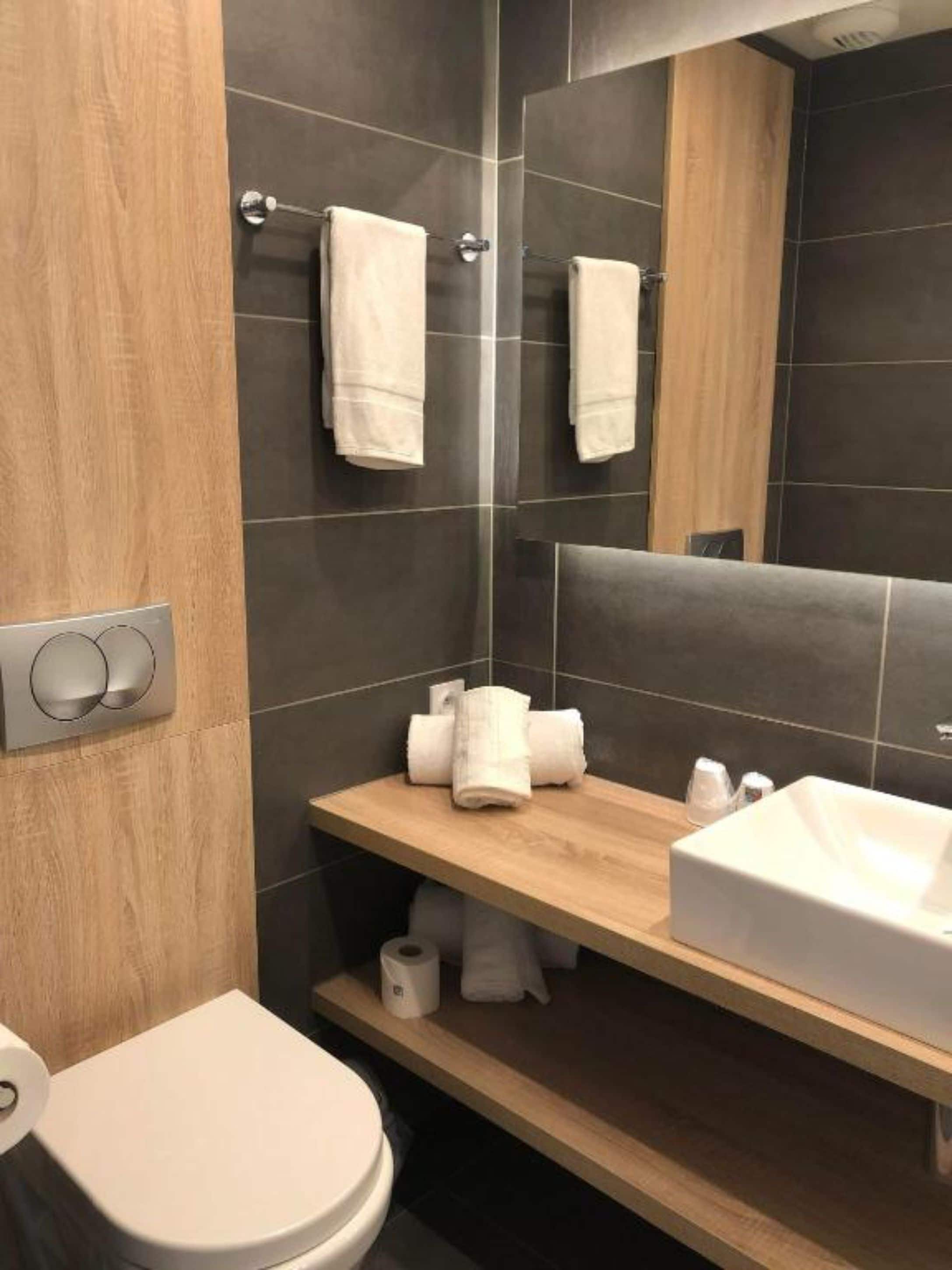 Een moderne badkamer met een houten wastafelmeubel, een witte wastafel en een toilet.