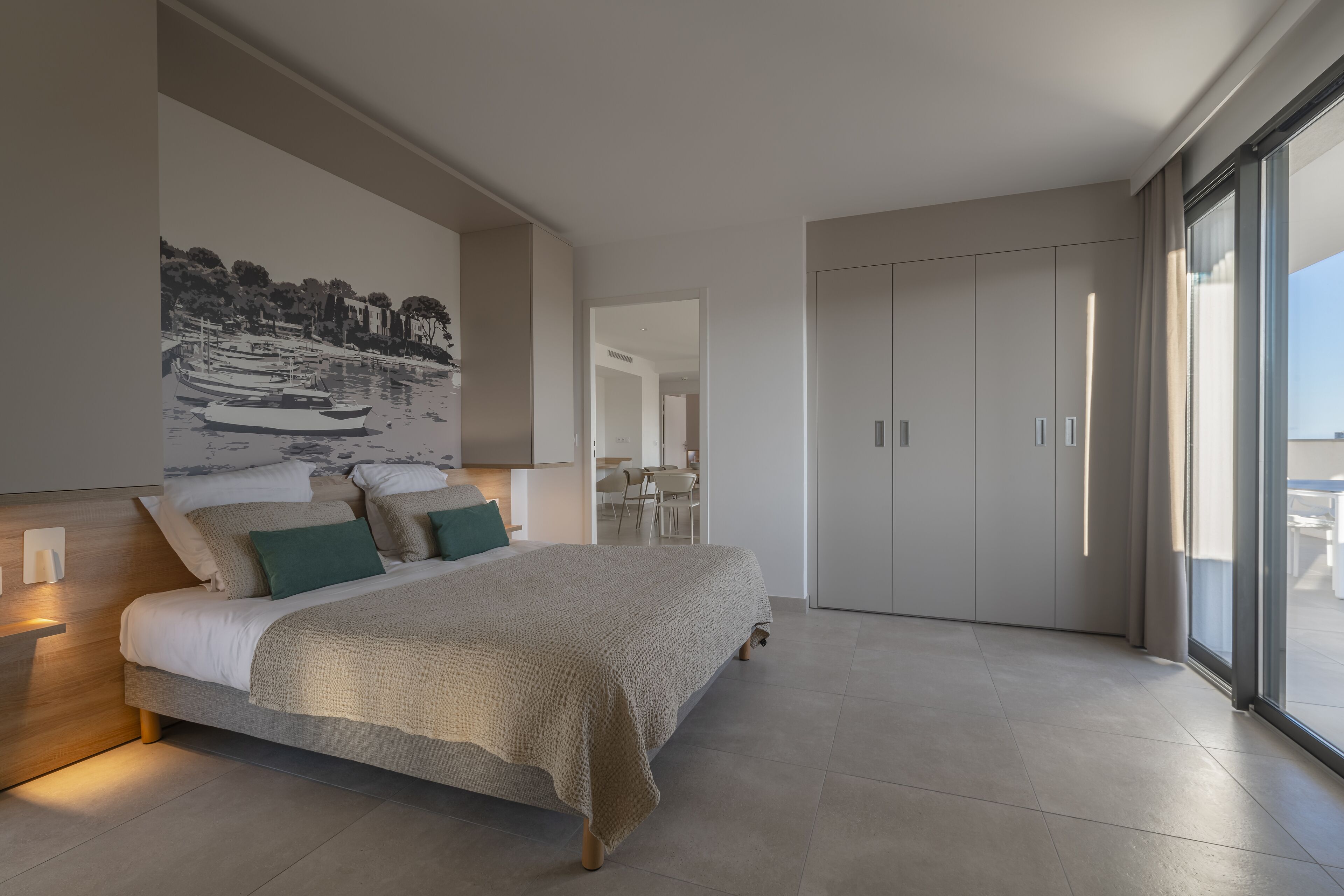 Une chambre moderne avec un grand lit, une œuvre d’art accrochée au mur et une porte coulissante donnant sur un balcon.