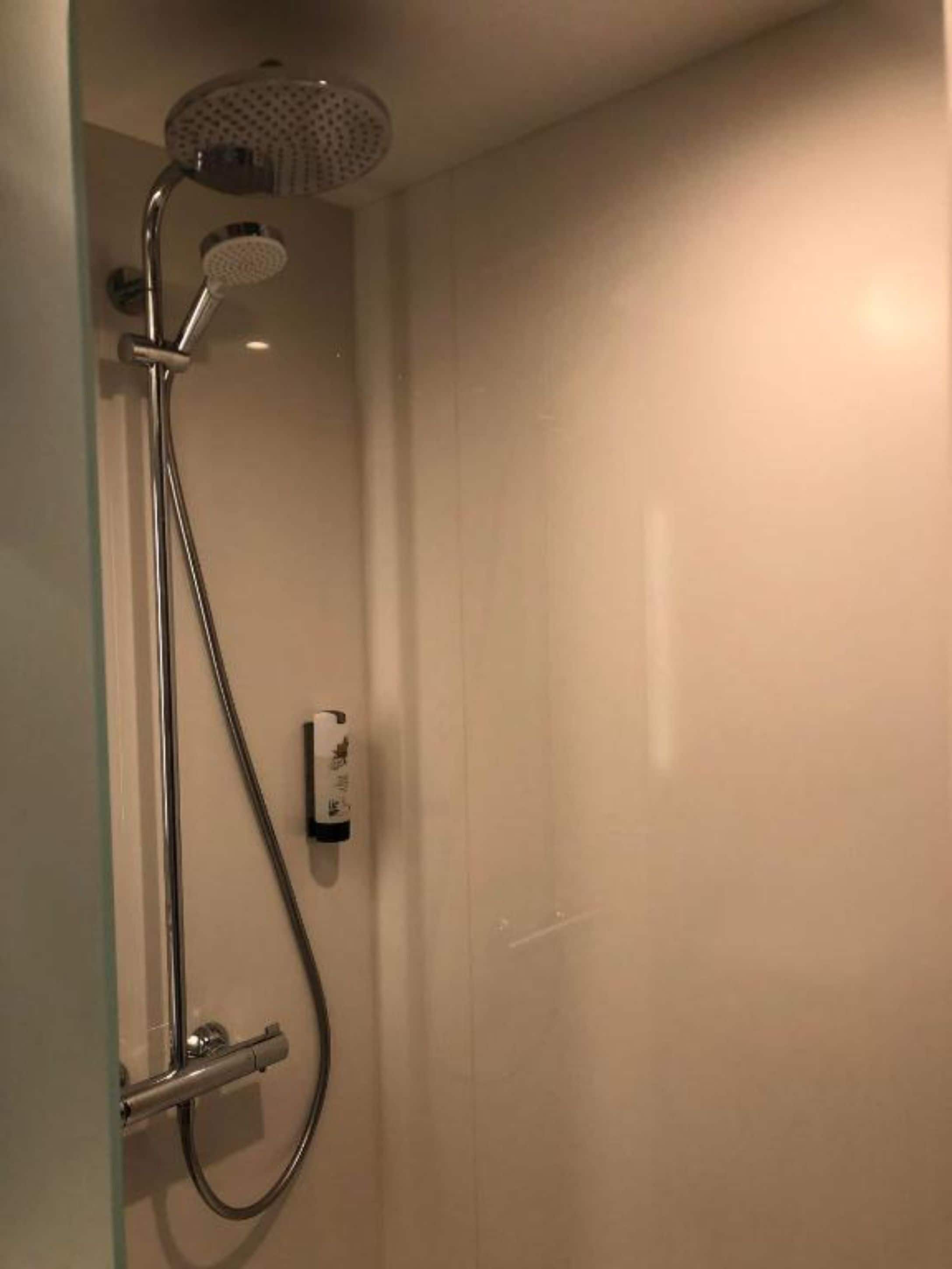 A shower with a handheld showerhead and a wall-mounted control panel.