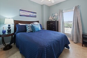 Quarto com uma cama grande, mesa de cabeceira com abajur, cômoda e janela com cortinas.