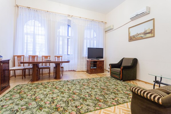 A living room with a dining table, chairs, a sofa, a TV, and a patterned rug.