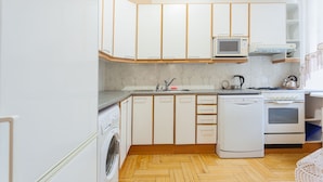 Une cuisine compacte avec des meubles blancs, un four à micro-ondes, une cuisinière et un lave-linge.