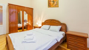 Un lit bien fait, avec du linge de lit et des serviettes blanches, une armoire en bois, une table de chevet avec une lampe et un tableau accroché au mur.