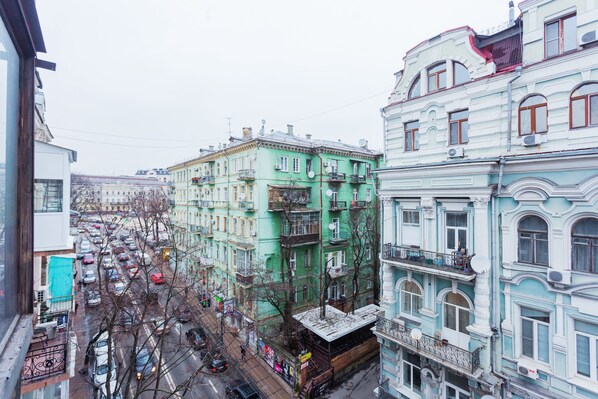 A street view with multi-story buildings, a busy road with cars, and bare trees.
