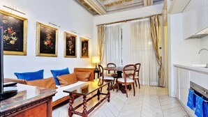 A hotel room with a sofa, a dining table with chairs, a TV, and a kitchen area.