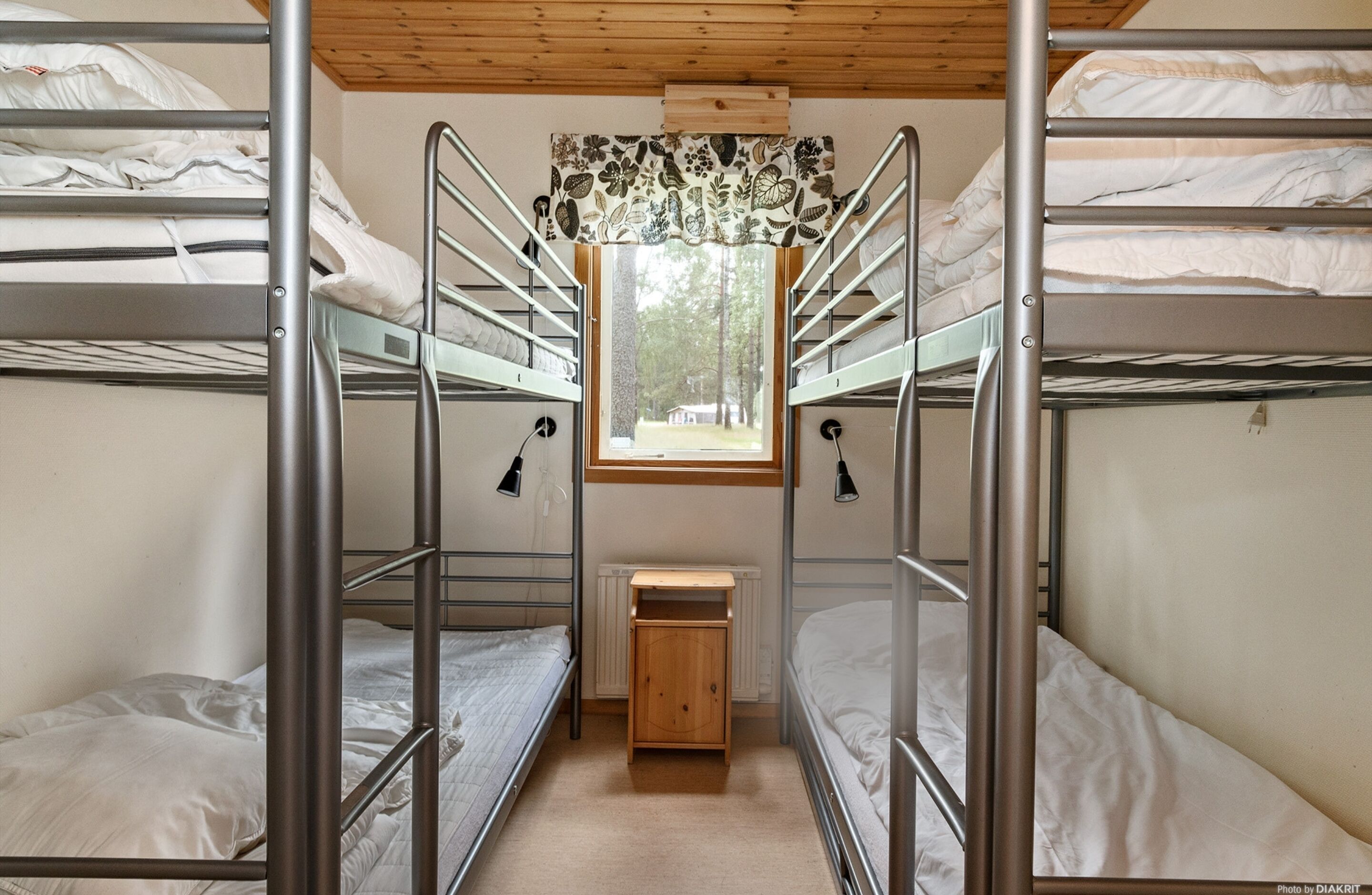 A bunk bed room with a window, a small wooden cabinet, and two wall-mounted lamps.