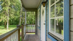 Une terrasse en bois avec une balustrade blanche, un porche couvert et une vue sur une zone boisée.