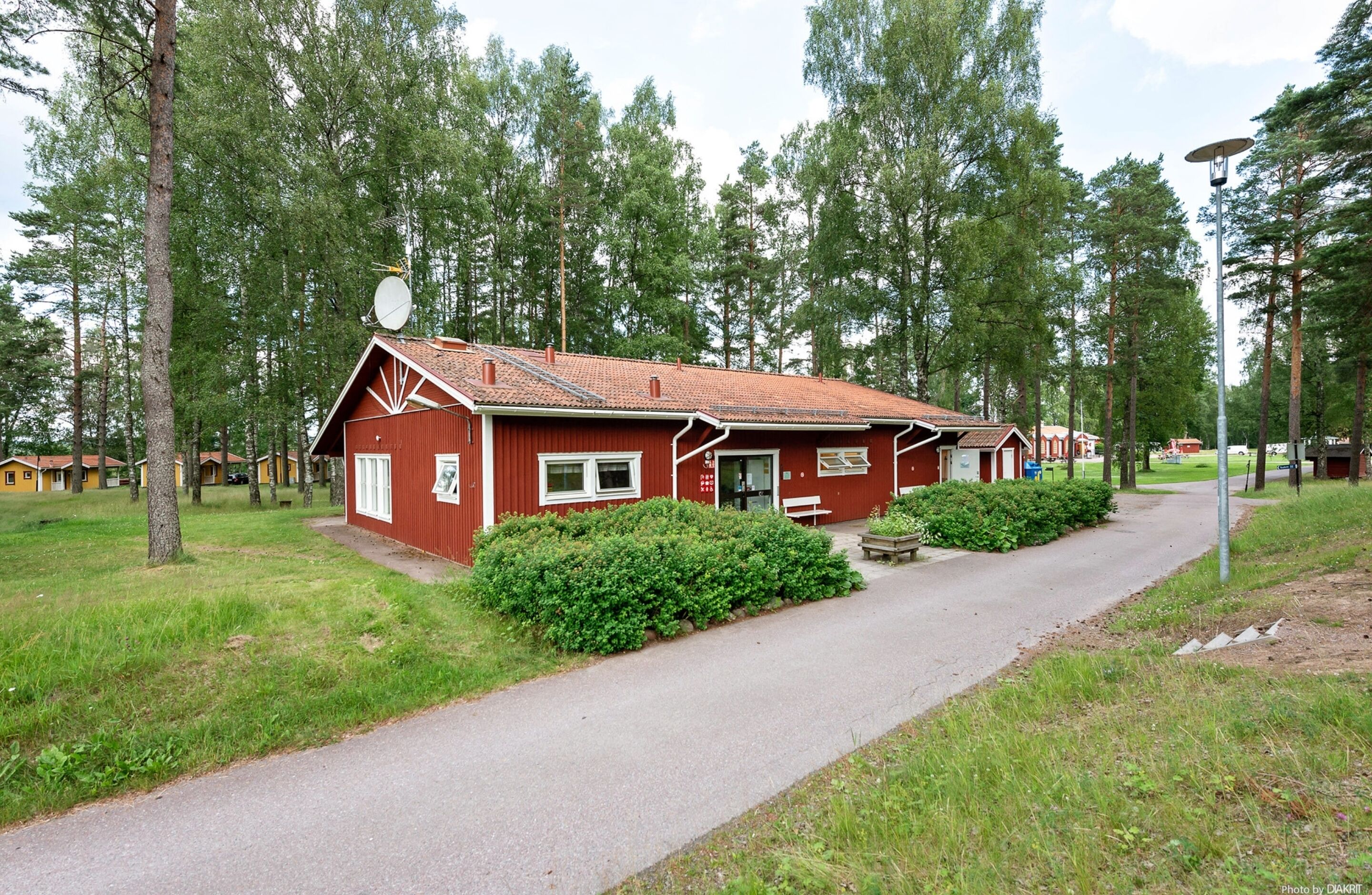 A red building with a sloped roof, surrounded by greenery and trees.