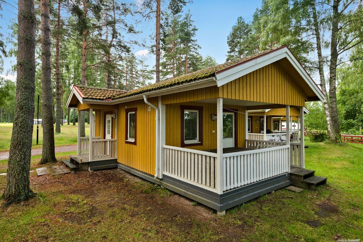 Une cabane jaune avec un porche, entourée d’arbres.