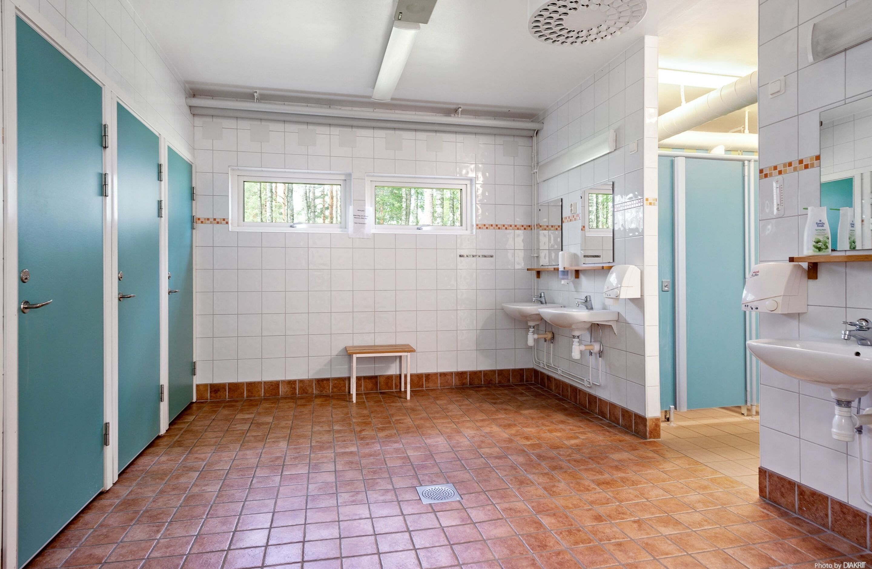 A bathroom with teal doors, white tiled walls, two windows, a bench, and a sink.