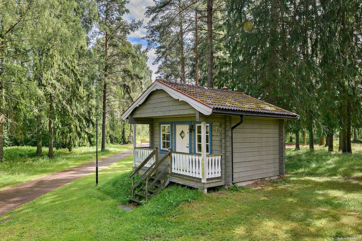 Une petite cabane en bois dotée d’un porche et d’un escalier, entourée d’arbres.