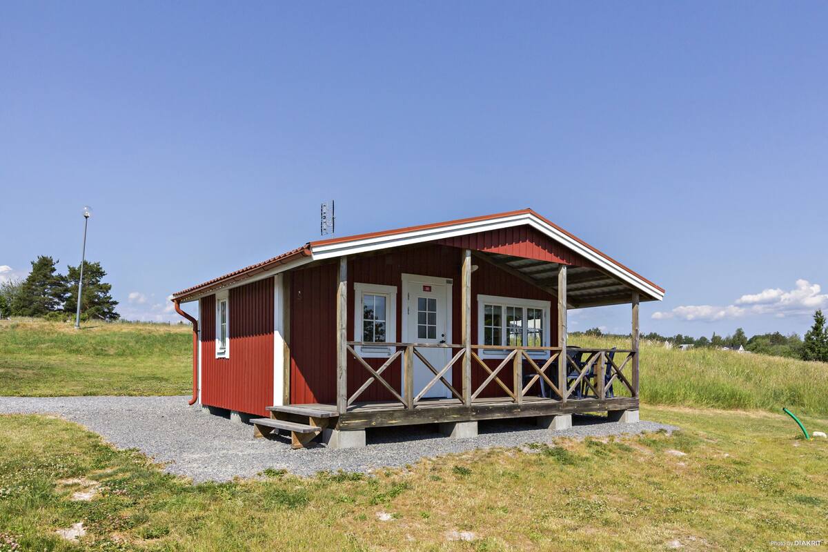 Eine rote Holzhütte mit Veranda, einem Schotterweg und einem grünen Feld im Hintergrund.