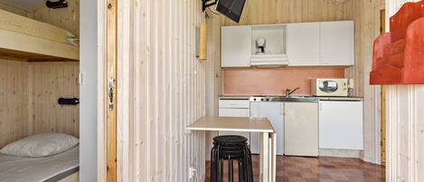 A compact room with a bunk bed, a small kitchenette, a dining table with chairs, and a television mounted on the wall.
