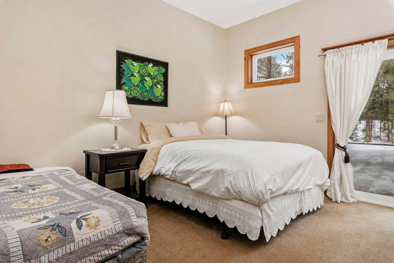 Um quarto com cama, mesa de cabeceira, abajur, janela com cortinas e um quadro na parede.