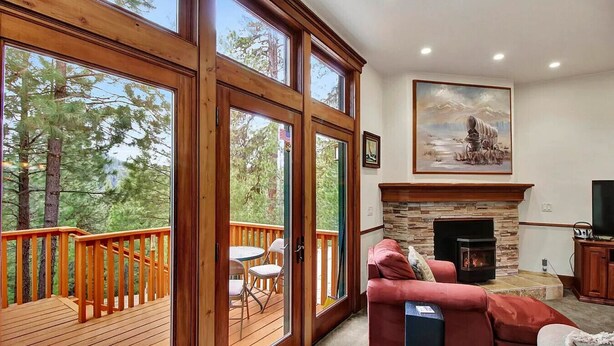 A spacious living room with a fireplace, a large window overlooking a deck, and a painting on the wall. - Smiths Ferry Cabin by Cabarton & Snowmobile Trails (Smiths Ferry)