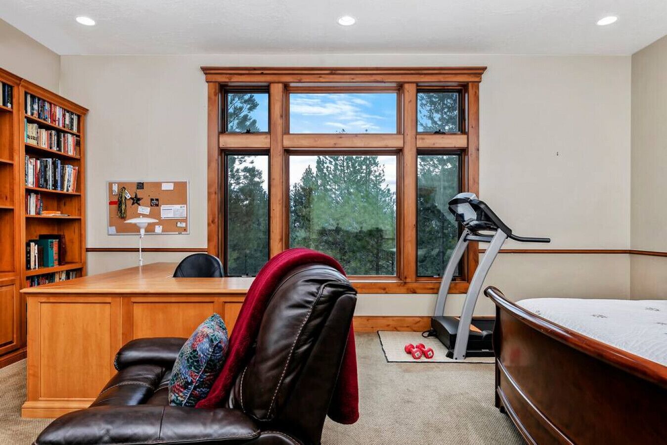 A home office with a desk, leather chair, treadmill, and a bookshelf.