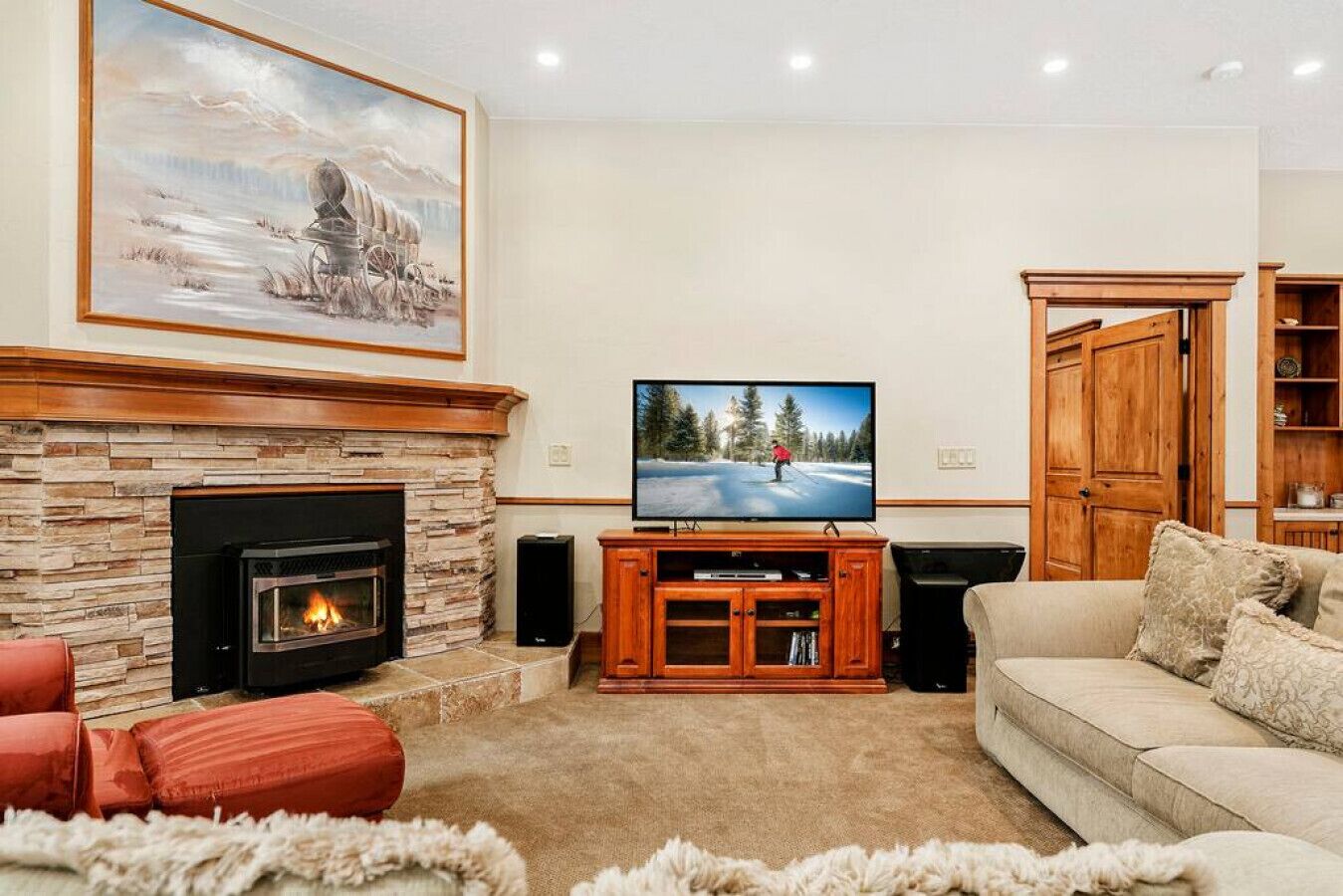 A living room with a stone fireplace, a television mounted on a wooden stand, a beige sofa, and a large painting above the fireplace.