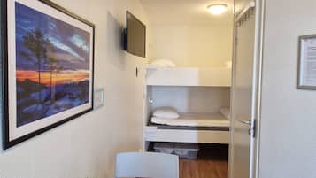 Une petite chambre comprenant un lit superposé, une petite table avec une chaise, un téléviseur fixé au mur et un tableau encadré accroché au mur.