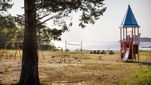 En strand med gyngestativ, volleyballnet, rutsjebane og picnicbord.
