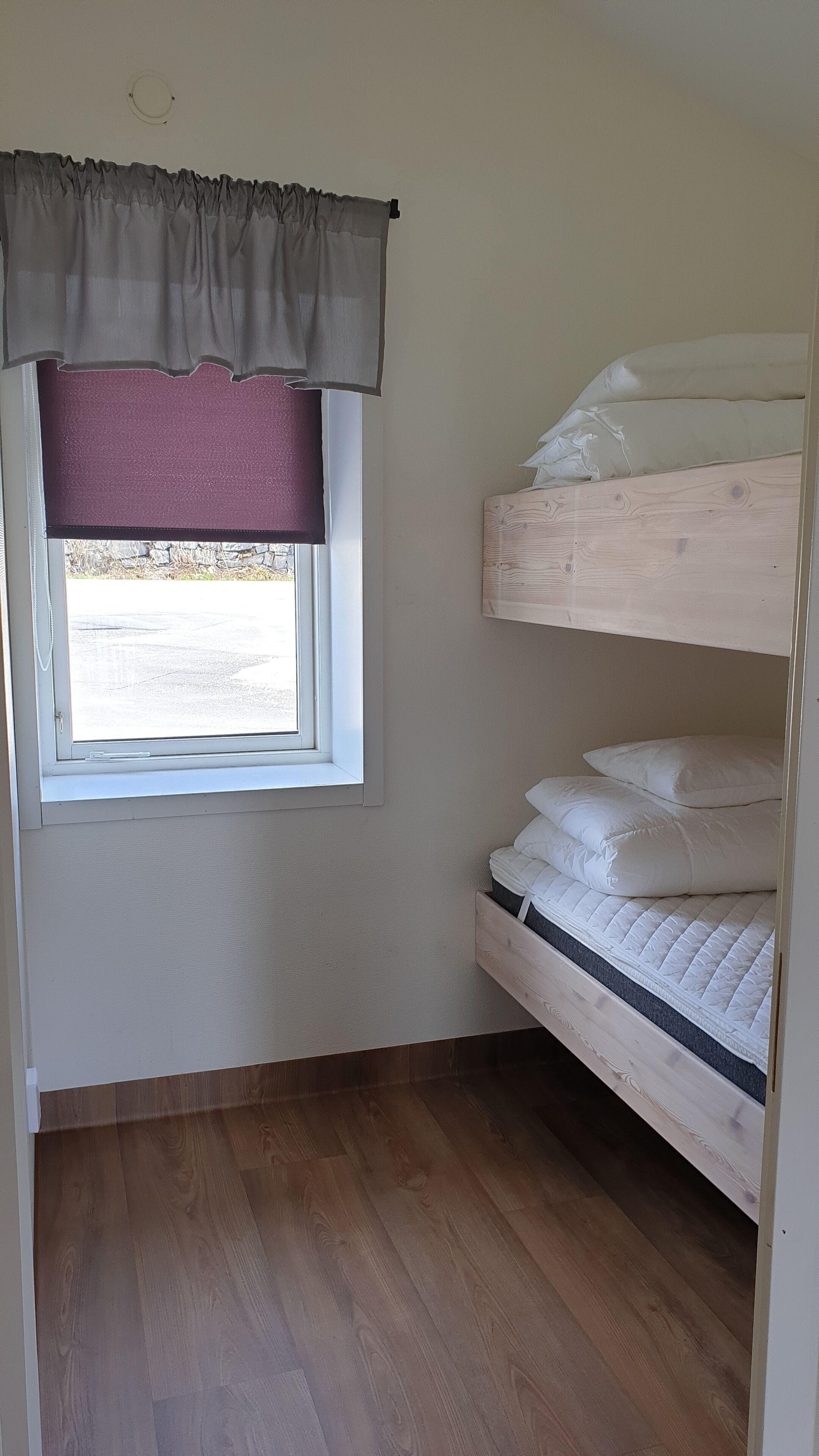Una habitación pequeña con cama individual, ventana, suelo de madera y cortina.