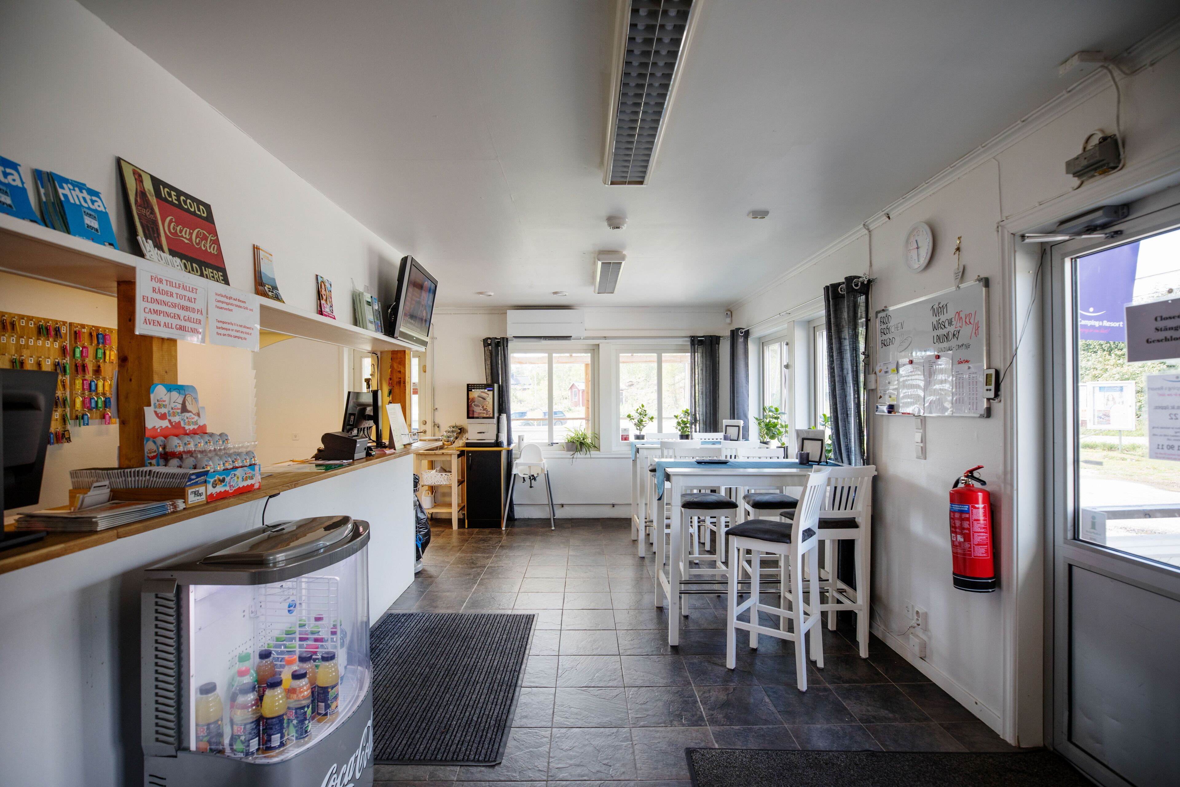 Una cocina con refrigerador, cafetera y zona de comedor con sillas y una mesa.