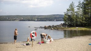 En strandscene med en redningskrans, sand og en rolig sø.