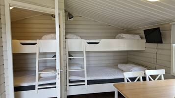 Quarto com beliche, escrivaninha e cadeira, televisão presa na parede e escada para acesso.