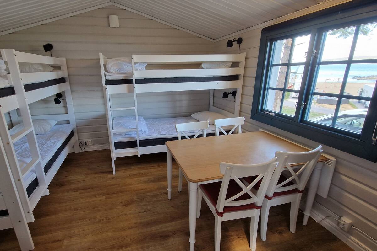 Een slaapzaal met stapelbedden, een houten tafel en stoelen.