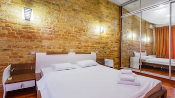 Hotelkamer met een bakstenen muur, een grote spiegel, een houten bed en een klein bureau met een stoel.