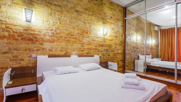 Une chambre d’hôtel avec un mur en briques, un grand miroir, un lit en bois et un petit bureau avec une chaise.
