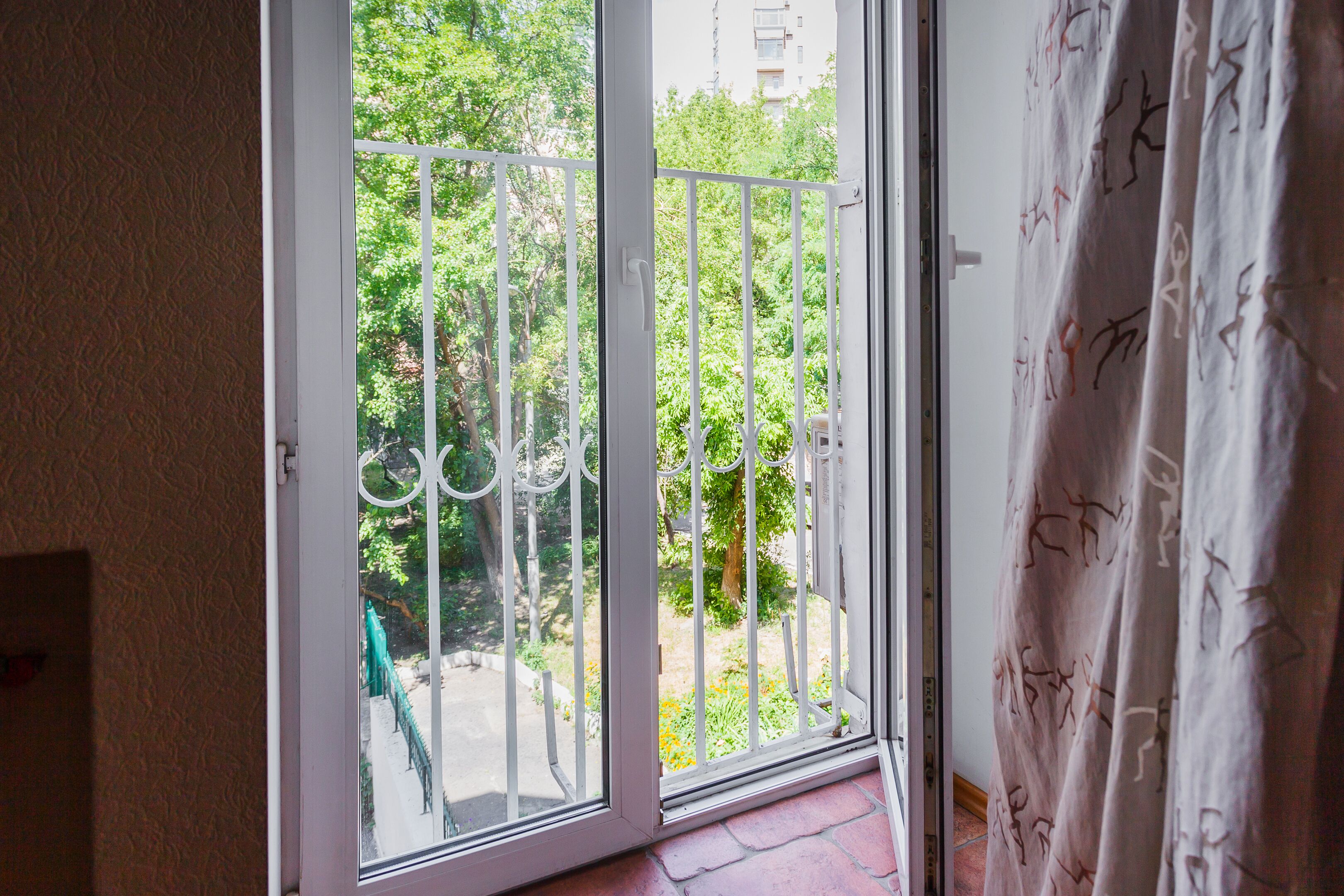 Een kamer met een schuifglazen deur die leidt naar een balkon met een metalen hekwerk en beplanting.