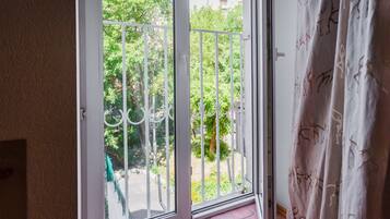 Een kamer met een schuifglazen deur die leidt naar een balkon met een metalen hekwerk en beplanting.