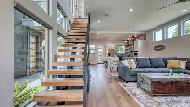 Un interior moderno con una escalera de madera, un sofá gris y una mesa de centro rústica.