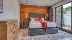 Une chambre avec un grand lit, des murs recouverts de panneaux de bois, un ventilateur de plafond et une vue sur l’extérieur, visible à travers une porte vitrée.